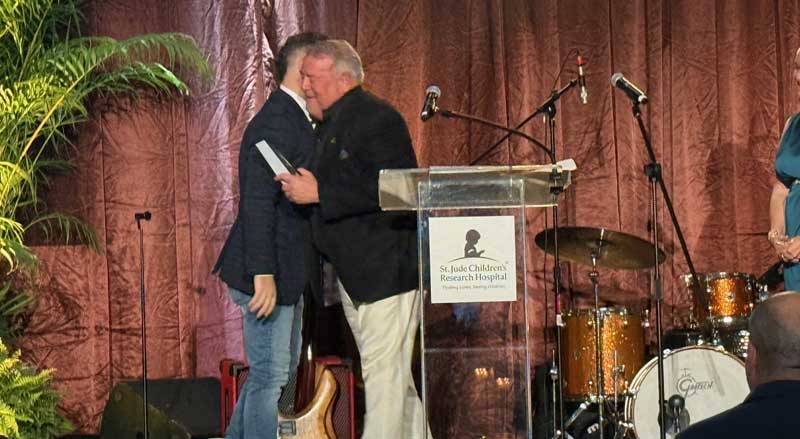 Speakers greeting on stage at the All In for St. Jude conference podium during a charity event supporting St. Jude Children’s Research Hospital.